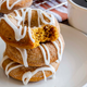 Stack of three pumpkin spice doughnuts with icing drizzle on a white plate beside a mug of coffee